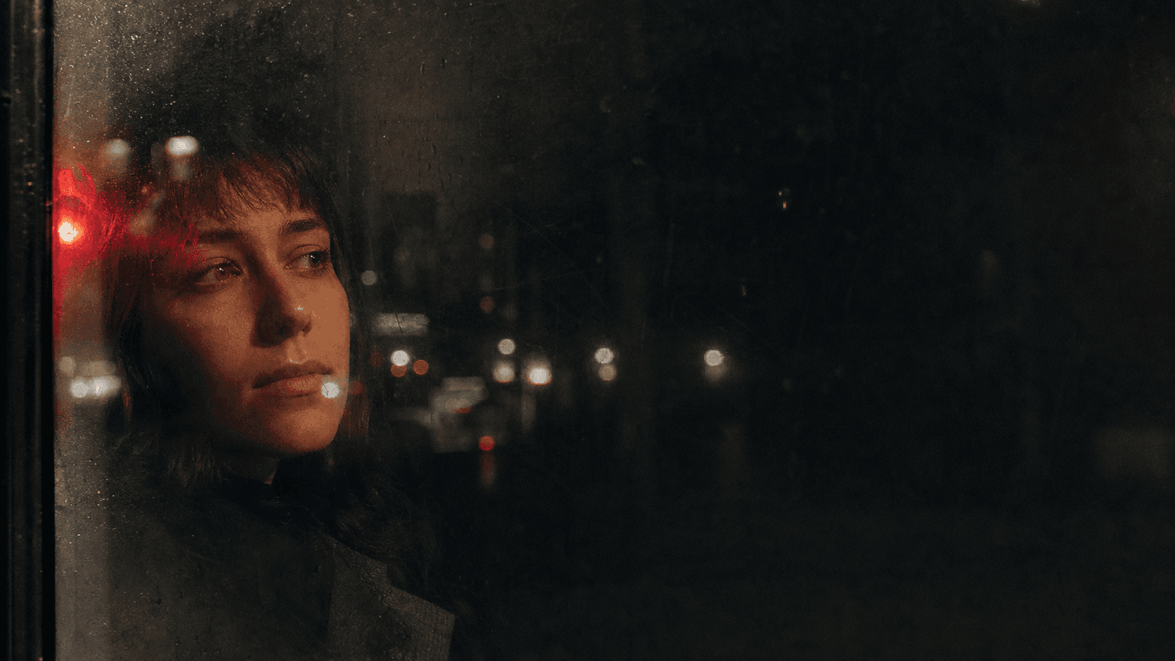 A contemplative person seen through a scratched window at night